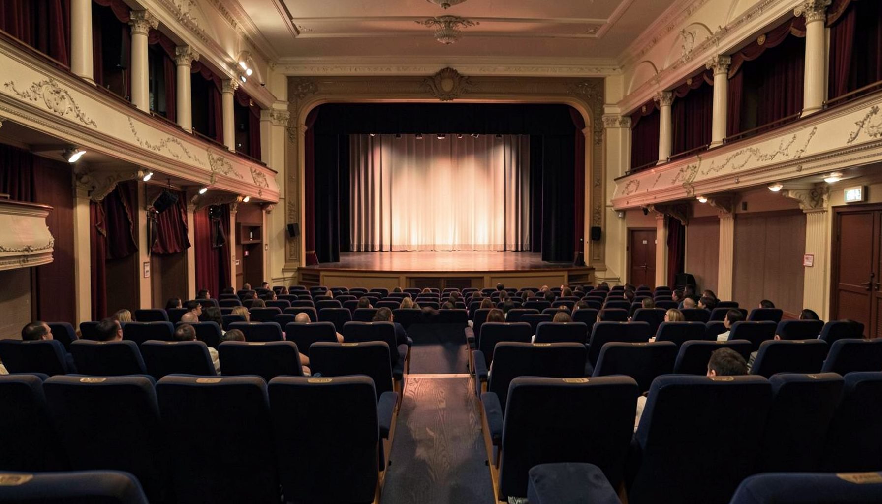 Classic theatre auditorium in navy and cream tones with rows of seating facing a lit stage, warm and welcoming mood