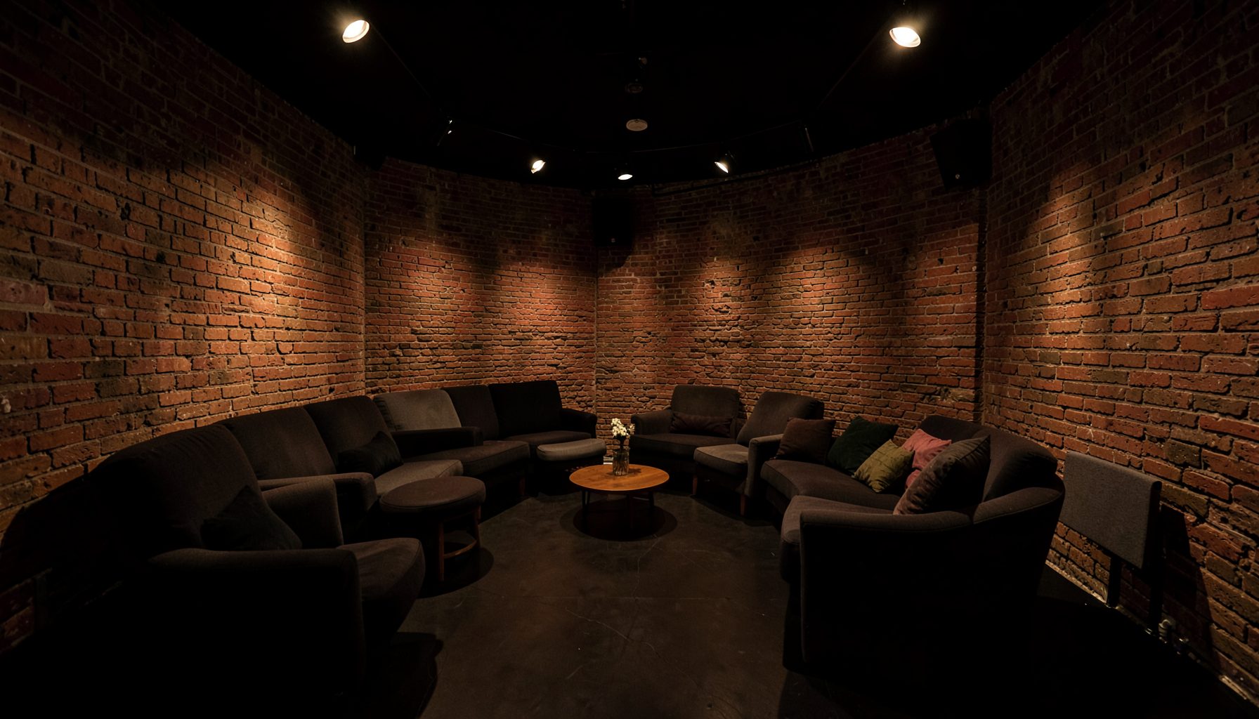 Intimate black-box theatre space with exposed brick walls, flexible seating, and warm track lighting creating a cosy atmosphere