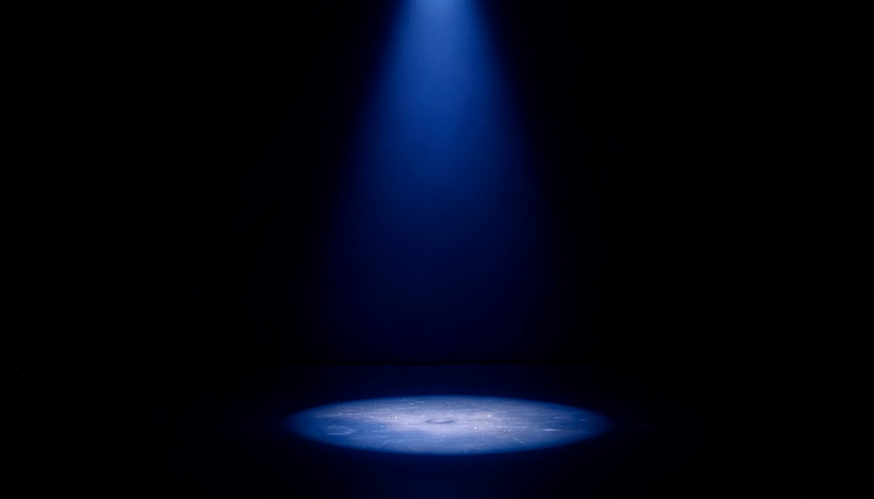 Single spotlight on an empty stage floor in deep indigo darkness, intimate and focused mood